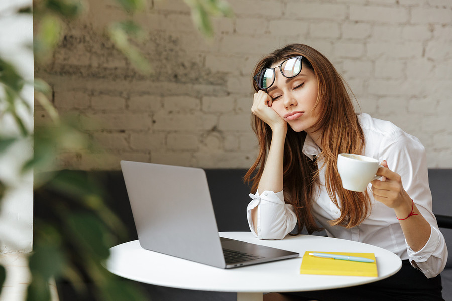 Portrait of a tired young businesswoman sitting at the table wit