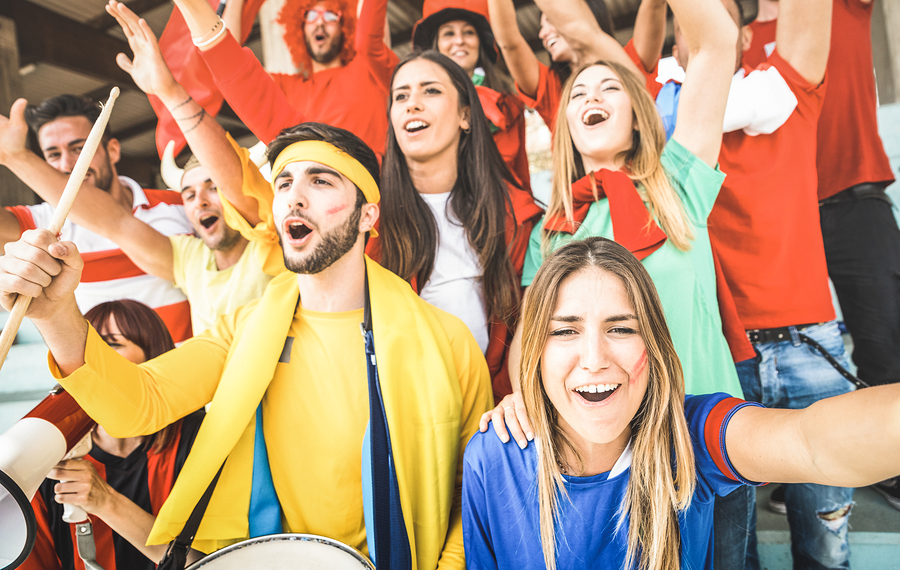 Young football supporter friends cheering and watching soccer cup match at intenational stadium - People fans group with multicolored t-shirts having excited fun on sport world championship concept