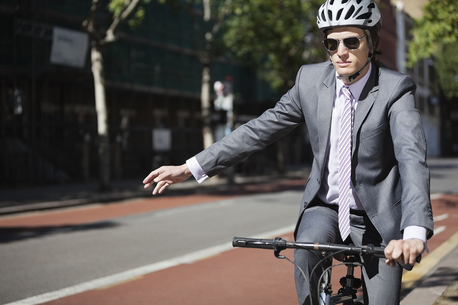Young businessman showing hand sign while riding bicycle