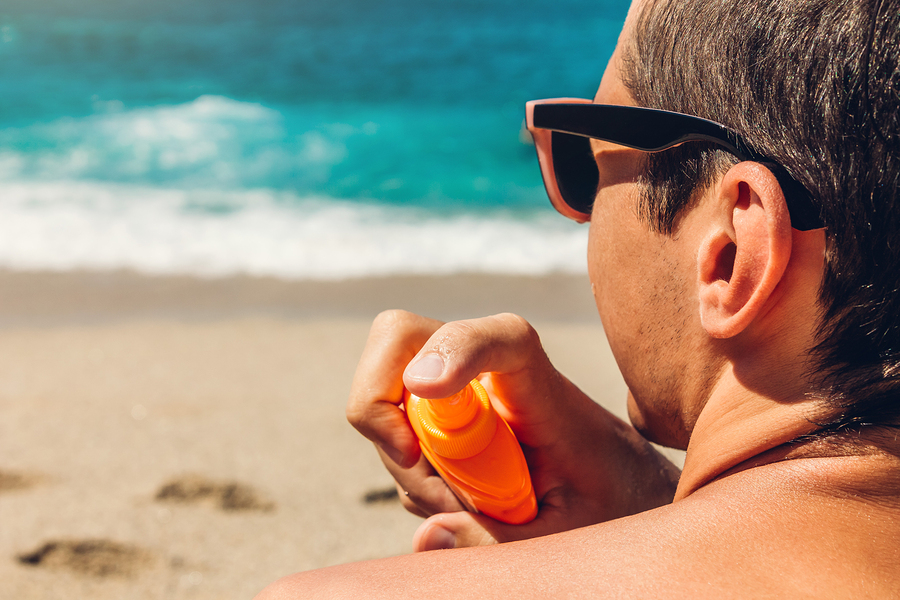 Sun cream protection. Man sprays sun cream on his shoulder on beach. Skin and body care concept. Healthy skin on vacation.