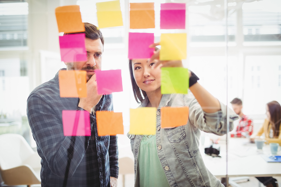 Creative business people looking at multi colored sticky notes on glass in meeting room at creative office