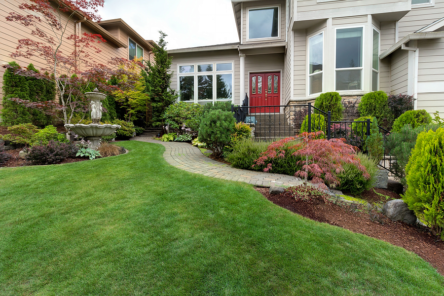 Frontyard garden of house with water fountain green grass lawn paver brick path trees and shrubs landscaping