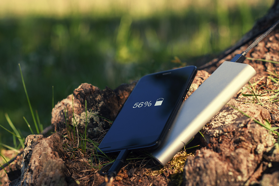 A portable charger charges the smartphone. Power Bank with cable against the background of wood and bicycle.