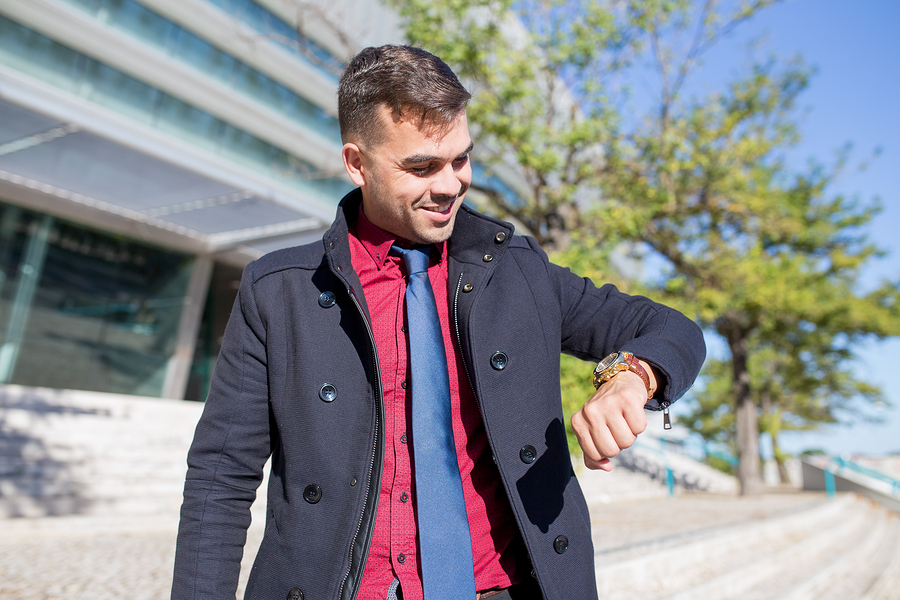 Portrait of happy young Caucasian businessman or student looking at watch and smiling outdoors. Education, business, punctuality concept