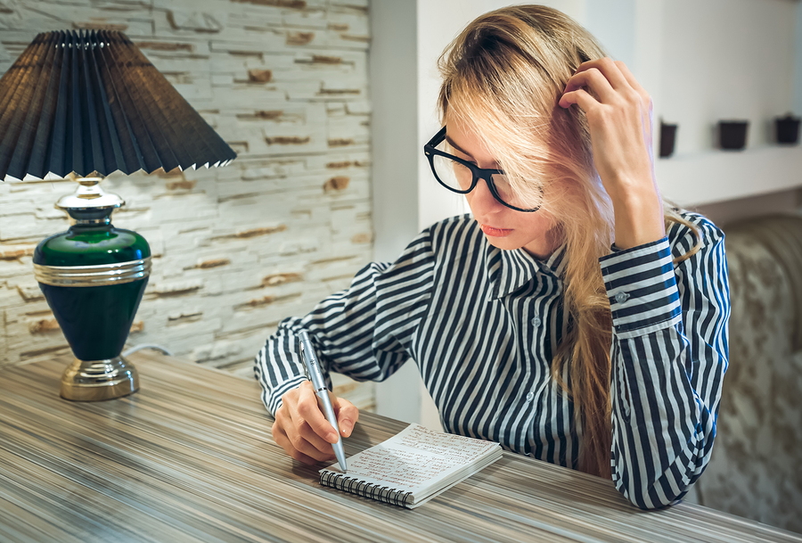 girl sitting at the table and writes in a paper notebook amounts to a list write poetry write down their thoughts and thinking