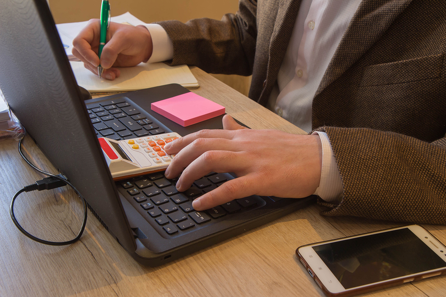 Pen on paperwork accounts with man use computer to save data in background. Man hand with pen, calculator and computer on wooden table. saving money or insurance concept