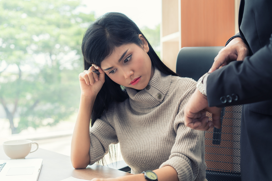 Angry business manager pointing his watch to subordinate businesswoman working missed deadline. Boss and worker at work having conflict.