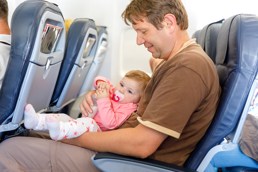 Father holding baby daughter during flight on airplane going on vacations. Baby girl drinking formula milk from bottle. Air travel with baby, child and family concept. Tired man traveling with kids