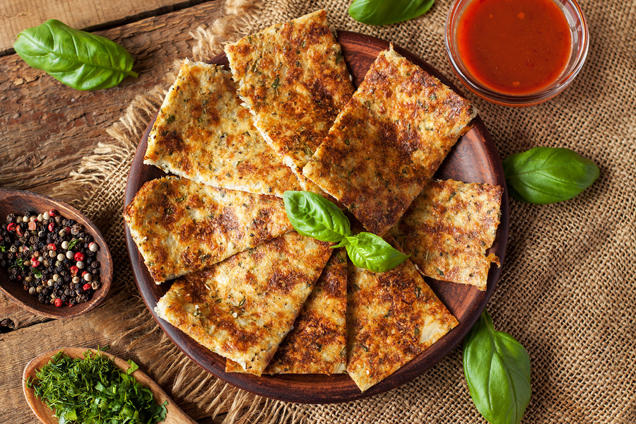 Breadsticks made of cauliflower, cheese and herbs, served with fresh basil leaves and red sauce