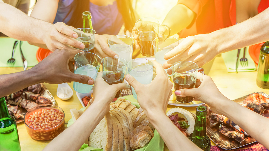 Group of friends toasting with aperitif eating barbecue outdoor - Closeup of hands cheering with cocktails and beers - Friendship summer fun and dinner concept - Soft focus on right bottom hand