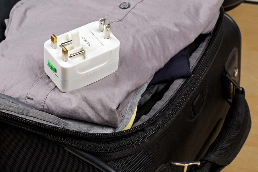 Travel power adapter with connectors for european UK and US power plugs on packed suitcase with clothings - travel preparation