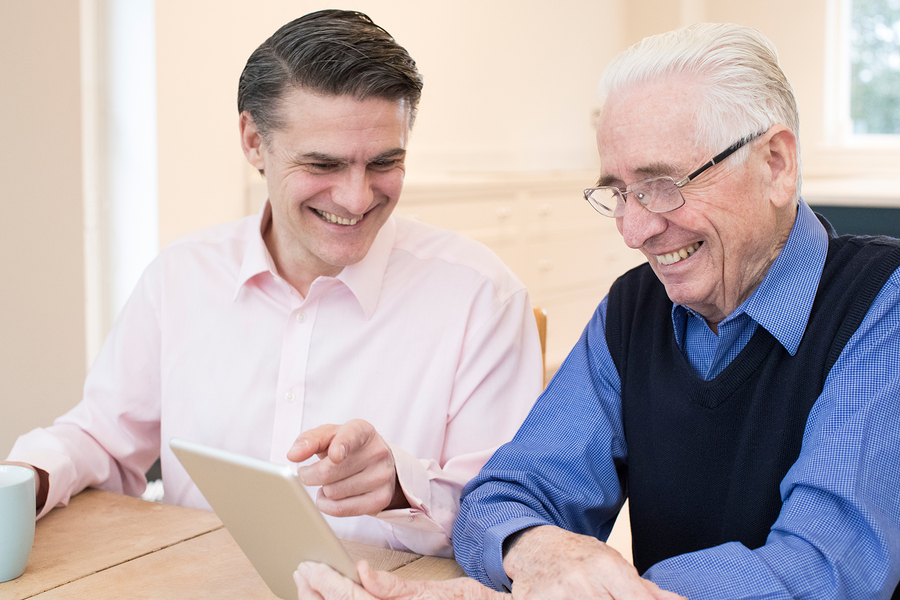 Male Neighbor Showing Senior Man How To Use Digital Tablet