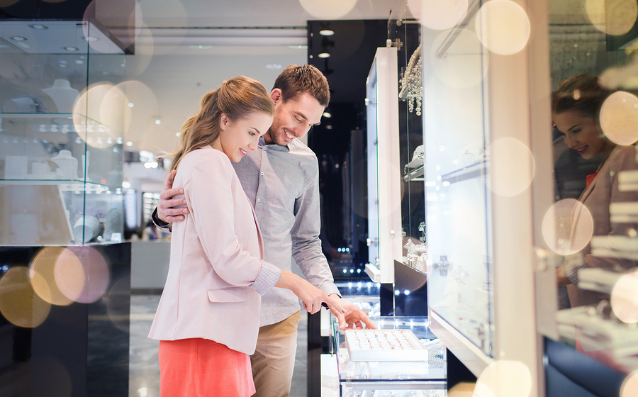 sale, consumerism, shopping and people concept - happy couple choosing engagement ring at jewelry store in mall