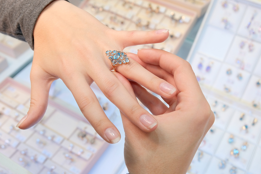 A girl in a jewelry store tries on her finger a gold ring with diamonds on the background of a shop window. Woman jeweler. Buying and shopping.