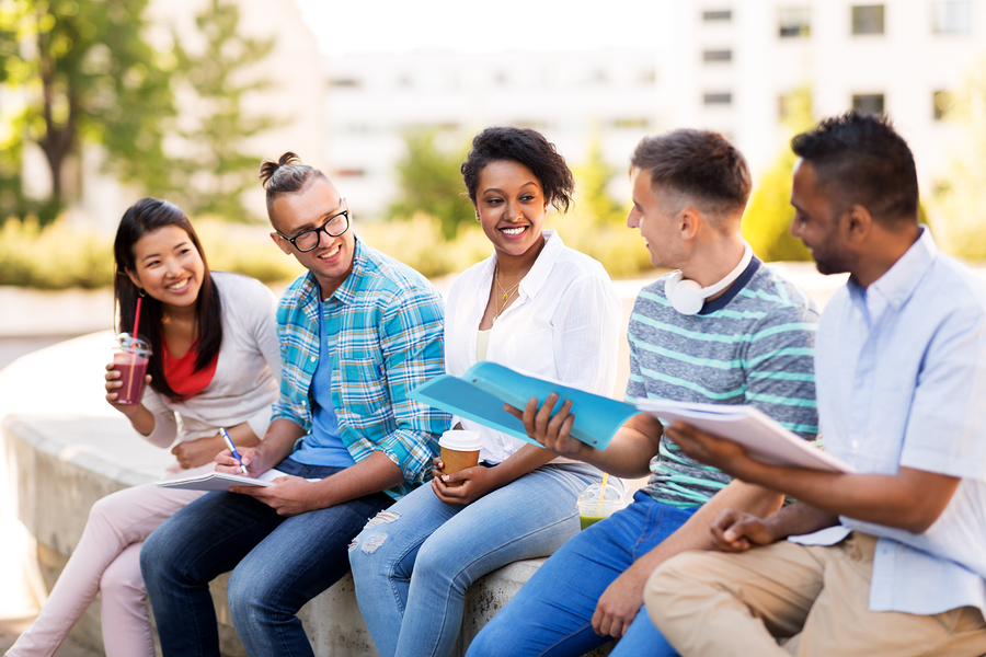 education, international and people concept - group of happy exchange students with notebook and takeaway drinks talking outdoors