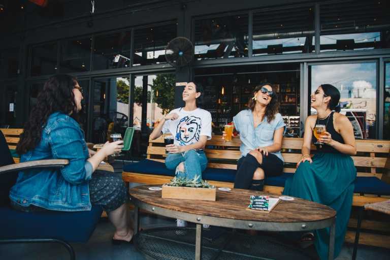 Four women sitting in a bench of a restaurant while laughing together.