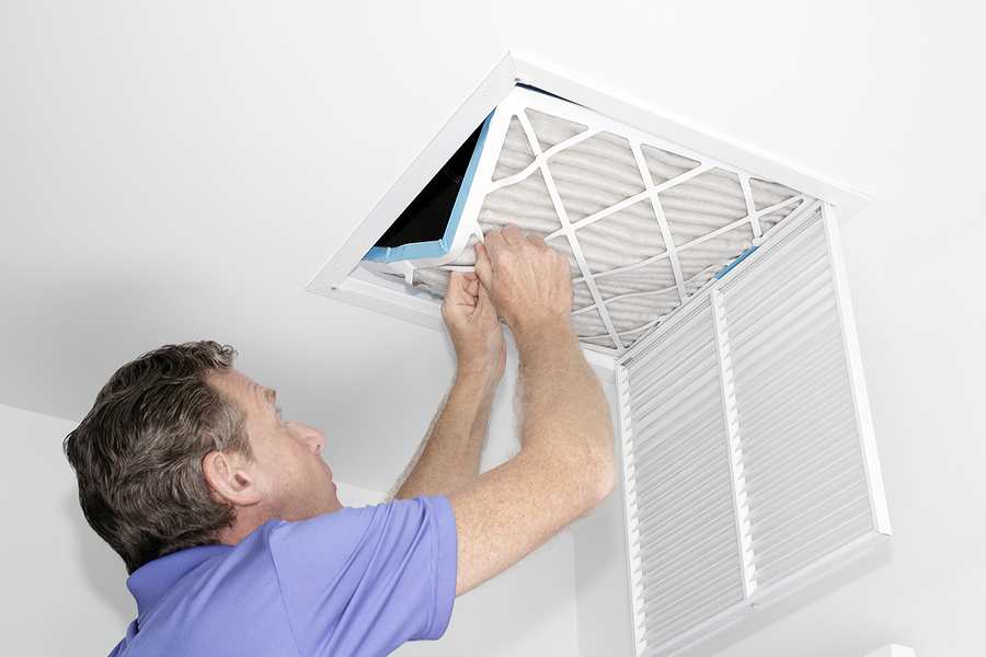 Man removing a dirty air filter in a house from a HVAC ceiling air vent.