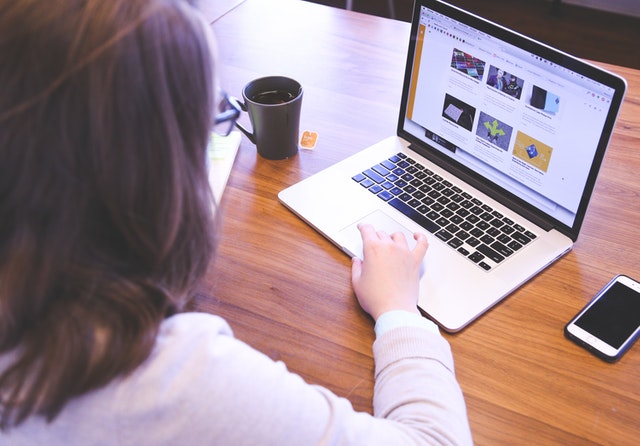 A woman with a cup of tea and a phone sitting in front of a laptop with her website for her mobile app open.