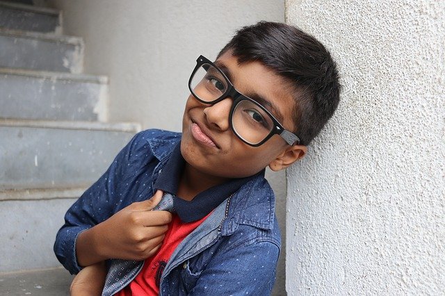 A boy wearing children's spectacle frames leaning against a wall.