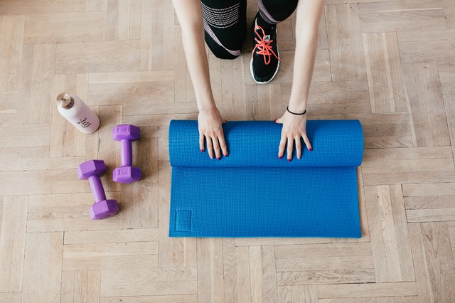 A person rolling up a yoga mat with other equipment from their home gym.