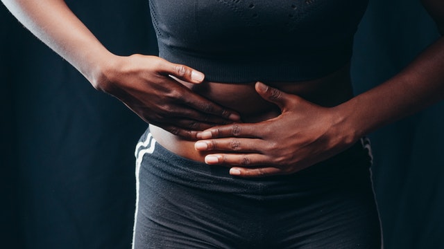 A woman standing holding her stomach because she has abdominal muscle separation.