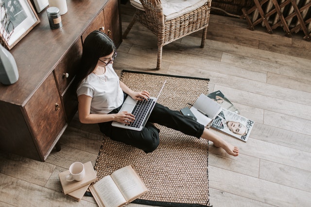 A woman on the floor writing as a part time blogger with magazines around her.
