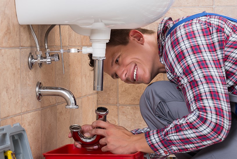 A plumber doing plumbing services on a sink in a bathroom.