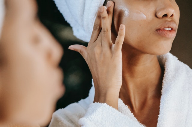 A woman putting moisturiser on her skin as part of her business meeting hair and makeup routine.